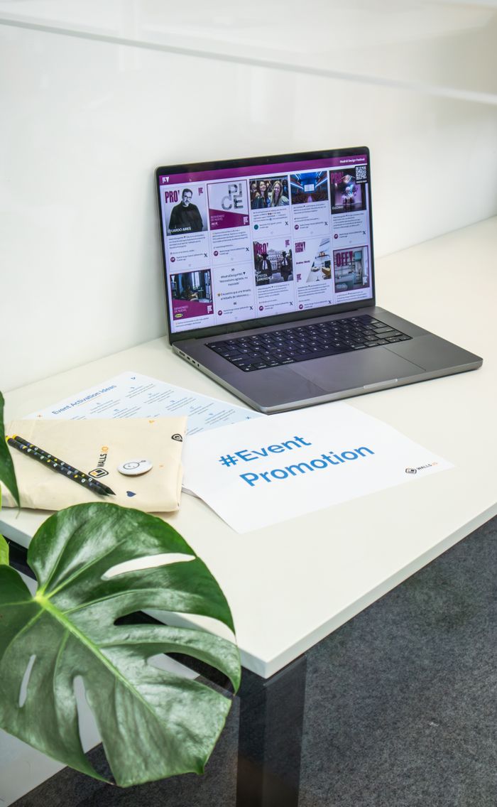 Espace de bureau épuré avec un ordinateur portable montrant des réseaux sociaux, des documents et une plante pour la promotion d’un événement.